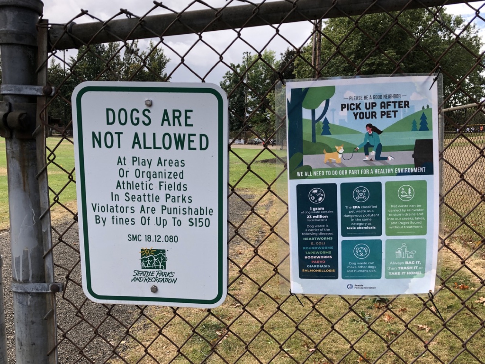Two signs on a chain-link fence: 'DOGS ARE NOT ALLOWED' next to 'PICK UP AFTER YOUR PET'